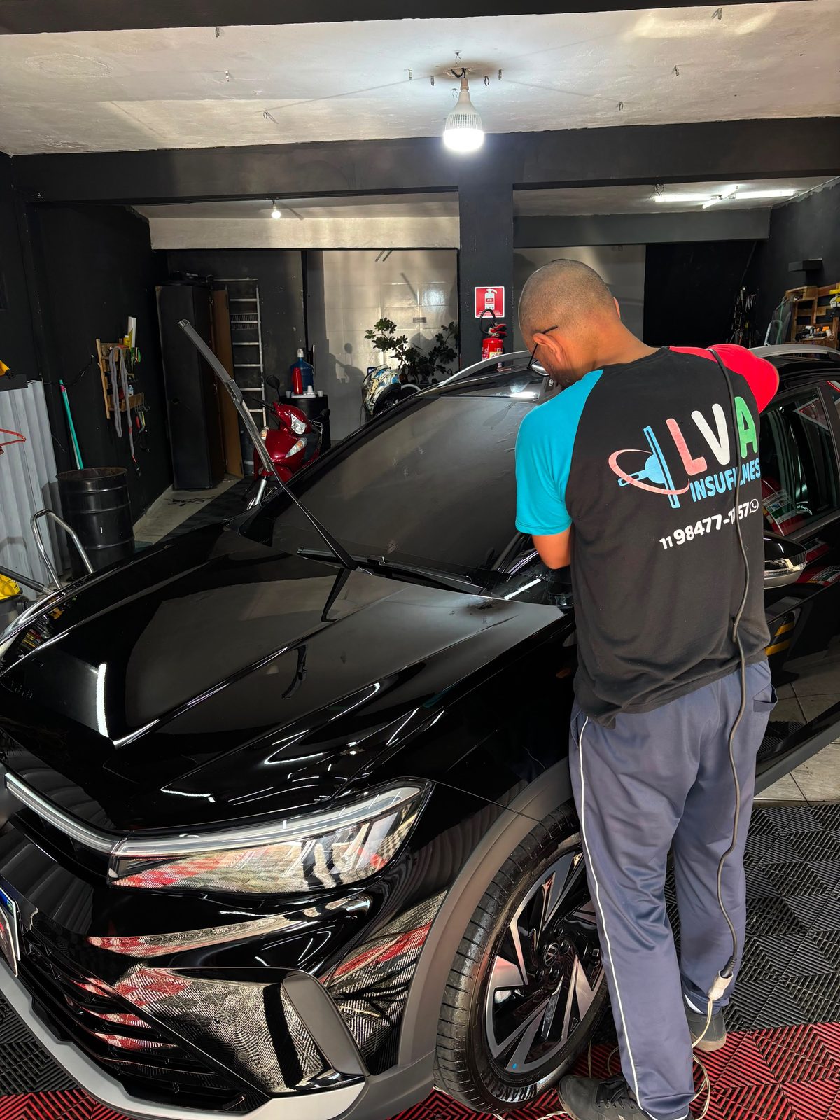 Aplicador da LVA Insufilmes instalando película em um carro preto na oficina, na Zona Sul de São Paulo